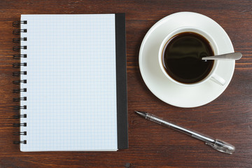 Cup of coffee, pen and opened notepad on desk. Top view