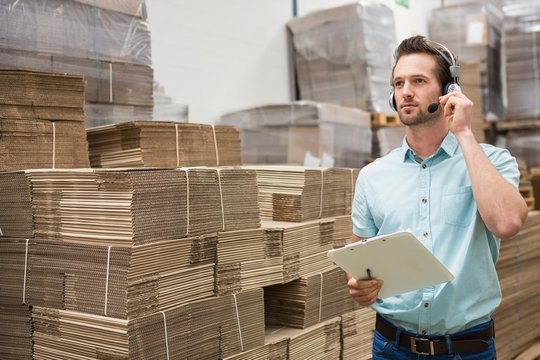 Warehouse worker wearing a headset holding clipboard - Powered by Adobe
