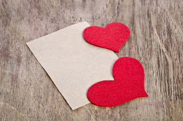 Two Red fabric hearts with sheet of paper on old wooden base