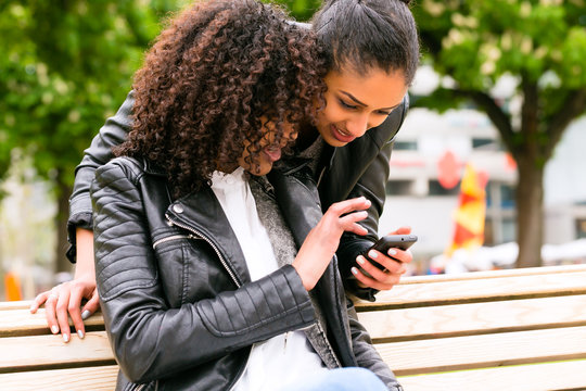 Beste Freunde chatten mit Smartphone auf Parkbank