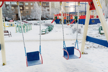 snow covered swing and slide at playground in winter
