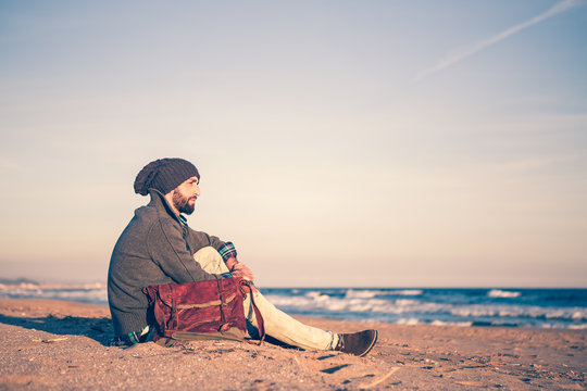Man sitting at the beach at sunset in winter