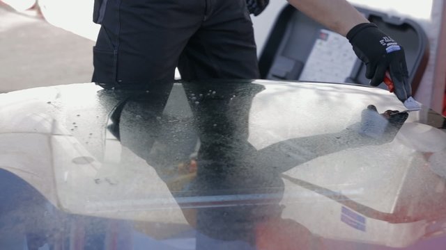 Male in working clothes cleaning windshield with scraper 