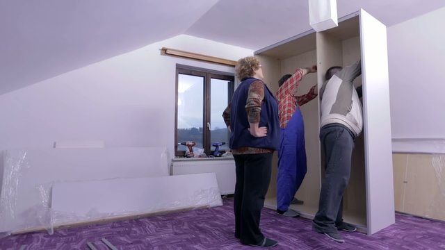 Older woman watches two guys assembling the wardrobe
