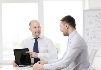 Obraz premium two smiling businessmen with laptop in office