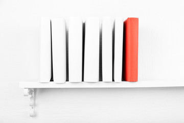 Blank books with red one on bookshelf on white wall background