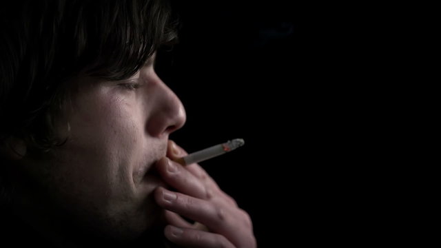 Side shot of young man inhaling a cigarette smoke in slo-mo