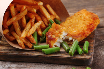 Breaded fried fish fillet and potatoes in paper bag with