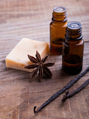 Bottles with aroma oil, vanilla pods and soap on the wooden back