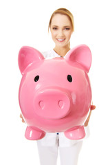 Young female doctor holding a piggybank.
