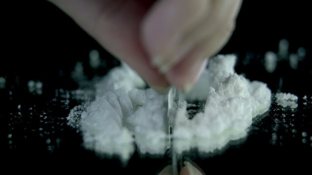 Preparing cocaine for sniffing on the black backgrond in slow motion