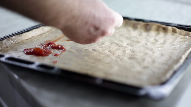 Close up shot of a black baking sheet with dough and a person who is putting on different kinds of ingredients for pizza