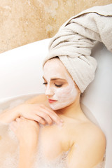 Woman relaxing in bathtub with face mask.