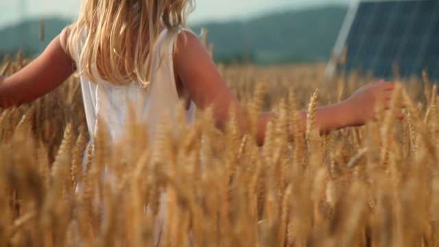 Little girl on a golden field with solar panels in the back