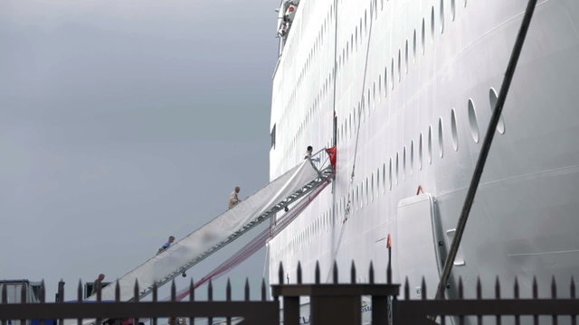 Shot of people ascending the stairs to board on white cruiser made behind fence