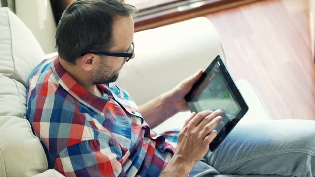 Man browsing photos on tablet computer sitting on sofa
