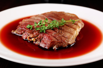 Grilled steak in wine sauce on plate on table close up