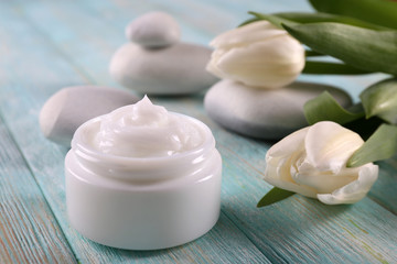 Cosmetic cream with flowers and spa stones on wooden background