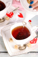 Woman pouring hot tea from teapot into cup wooden background