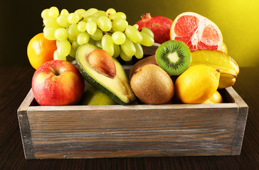 Assortment of fruits in box on dark yellow background