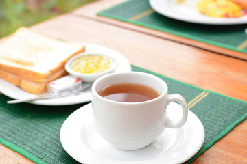 Hot tea in white cup with sliced bread on green mat