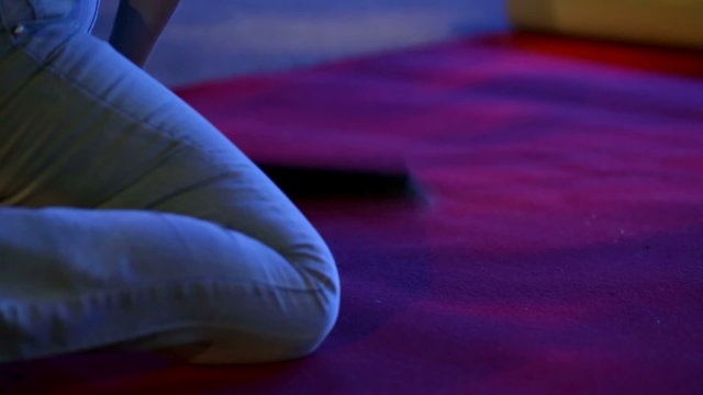 Woman is cleaning the red carpet with the mistletoe while on her knees