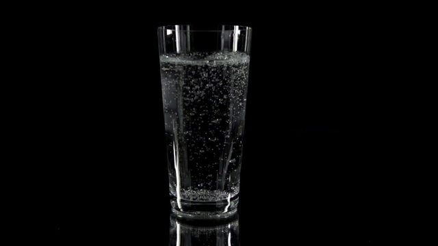 A glass full of sparkling water on black background