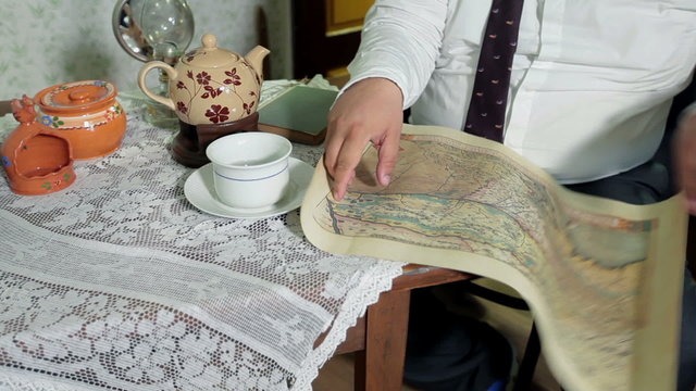 Man with a tie unrolls a scroll and starts to look at old map