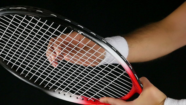 tennis player's hand adjusting the net of his tennis racket