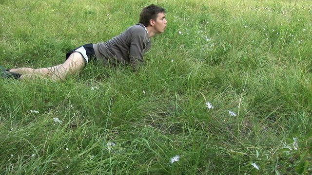 Guy is crawling in the grass while his friend walks by ruining his cover