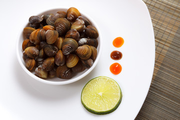 A plate with uncooked mussels and lime with sauces on a brown