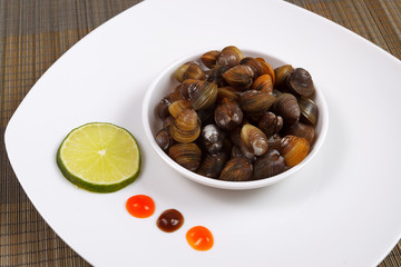 A plate with uncooked mussels and lime with sauces on a brown