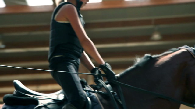 Close up on young girl riding horse in big hall
