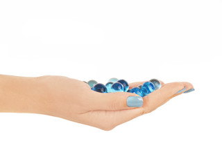 Mano de mujer sostenienco cápsulas azules sobre fondo blanco liso y aislado. Vista de frente. Copy space