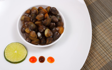 A plate with uncooked mussels and lime with sauces on a brown