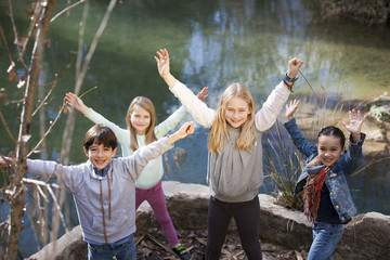 Niños junto a río levantando los brazos - obrazy, fototapety, plakaty