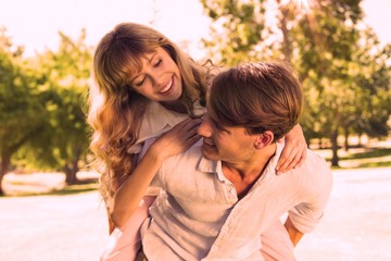 Fototapeta premium Man giving his pretty girlfriend a piggy back in the park