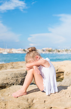 Sad little girl sitting on the beach. Place for text.