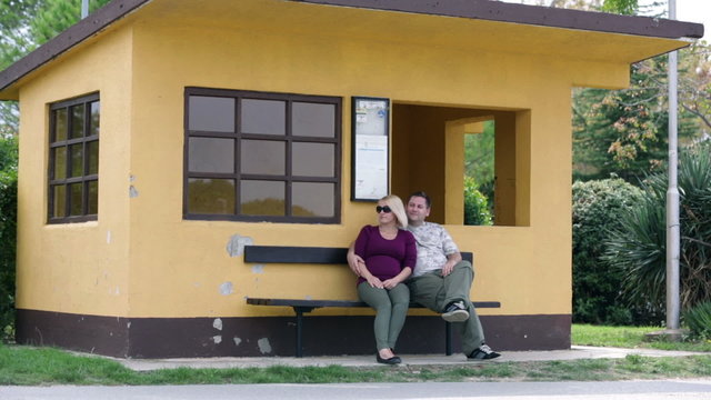 Couple sitting on bench in front of orange house
