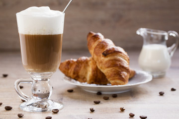 a cup of cappuccino with croissant and milk