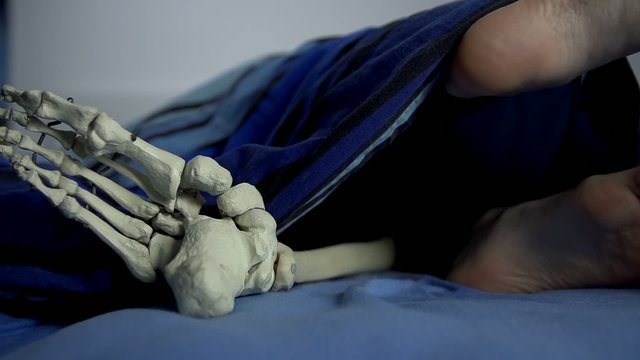 Human and skeleton's feet in the same bed