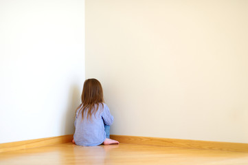 Sad little girl sitting in a corner