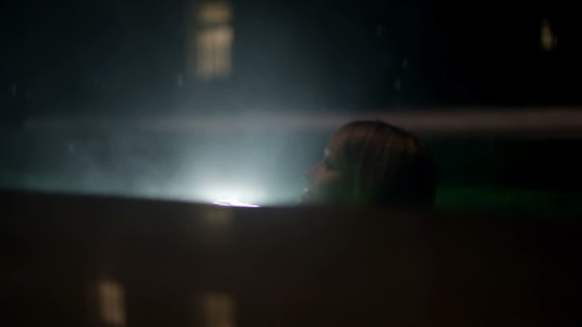 Shot of snowflakes falling in the outdoor pool in the night and a young woman swimming past the camera