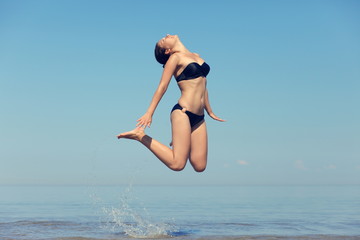 Beautiful young girl jumping on sea