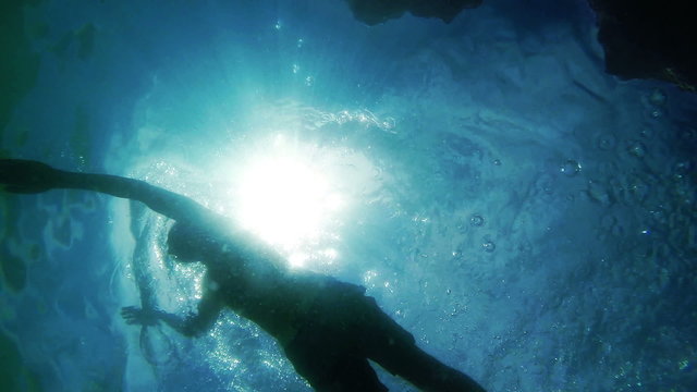 Swimming man silhouette with sun rays from bottom camera