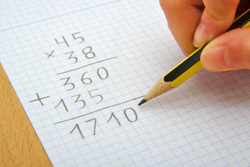 Hand of a child making a multiplication with a pencil. Math