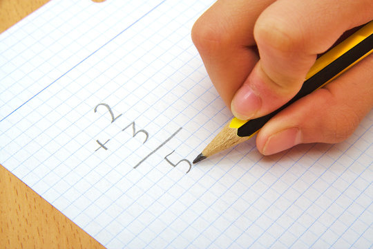 Hand of a child making a sum. Math. School concept.