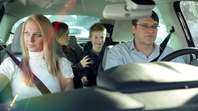 a young, beautiful and frightened family with two children who are having fun back in the car, while driving in a car to a certain destination