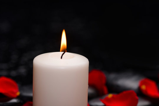 red rose petals with white candle and therapy stones