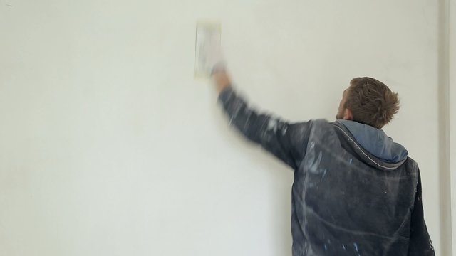 Man plasterers wall with plasterer's trowel, aligns sandpaper
